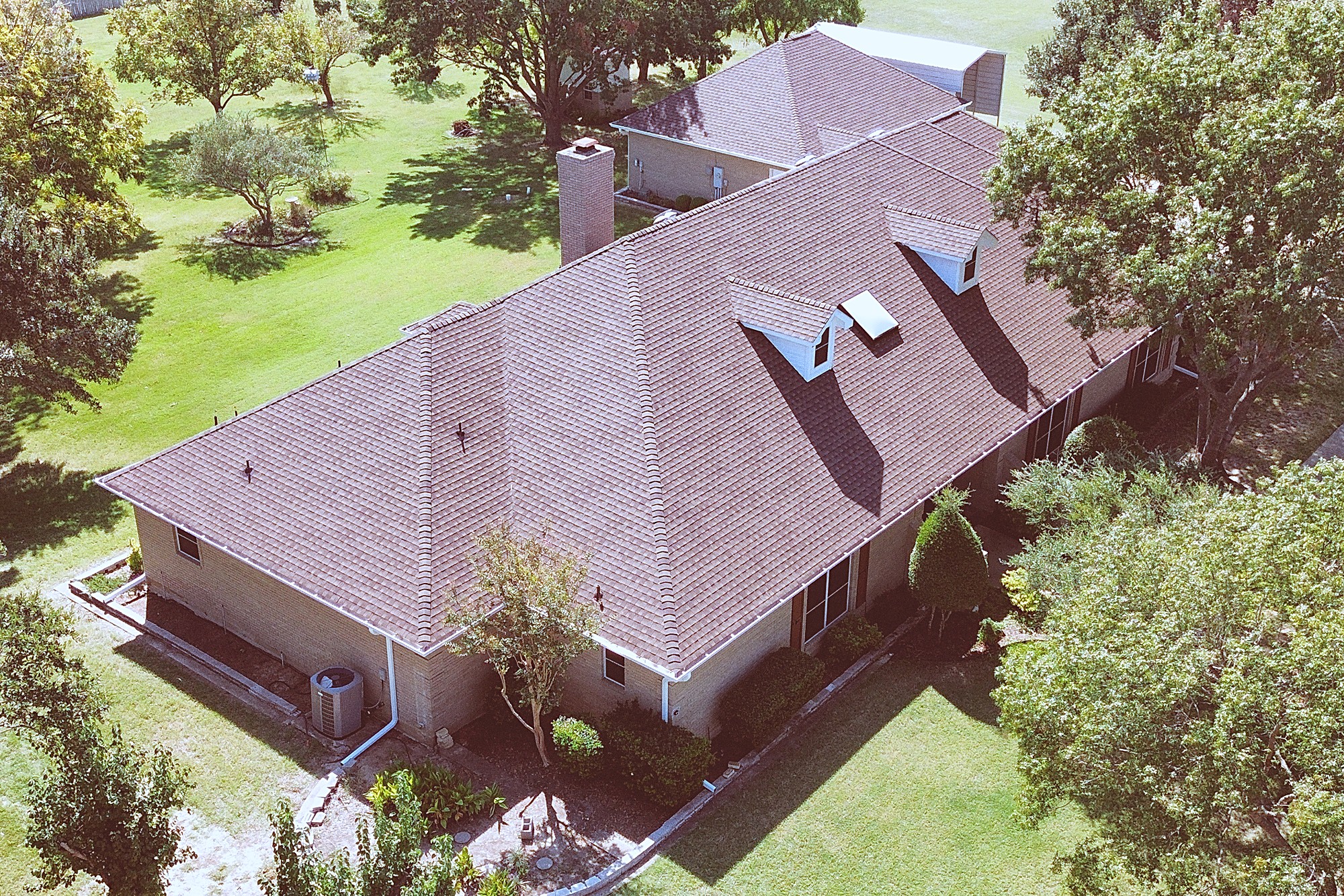 Aerial view of a long brick ranch home with dormers and a brown shingle roof