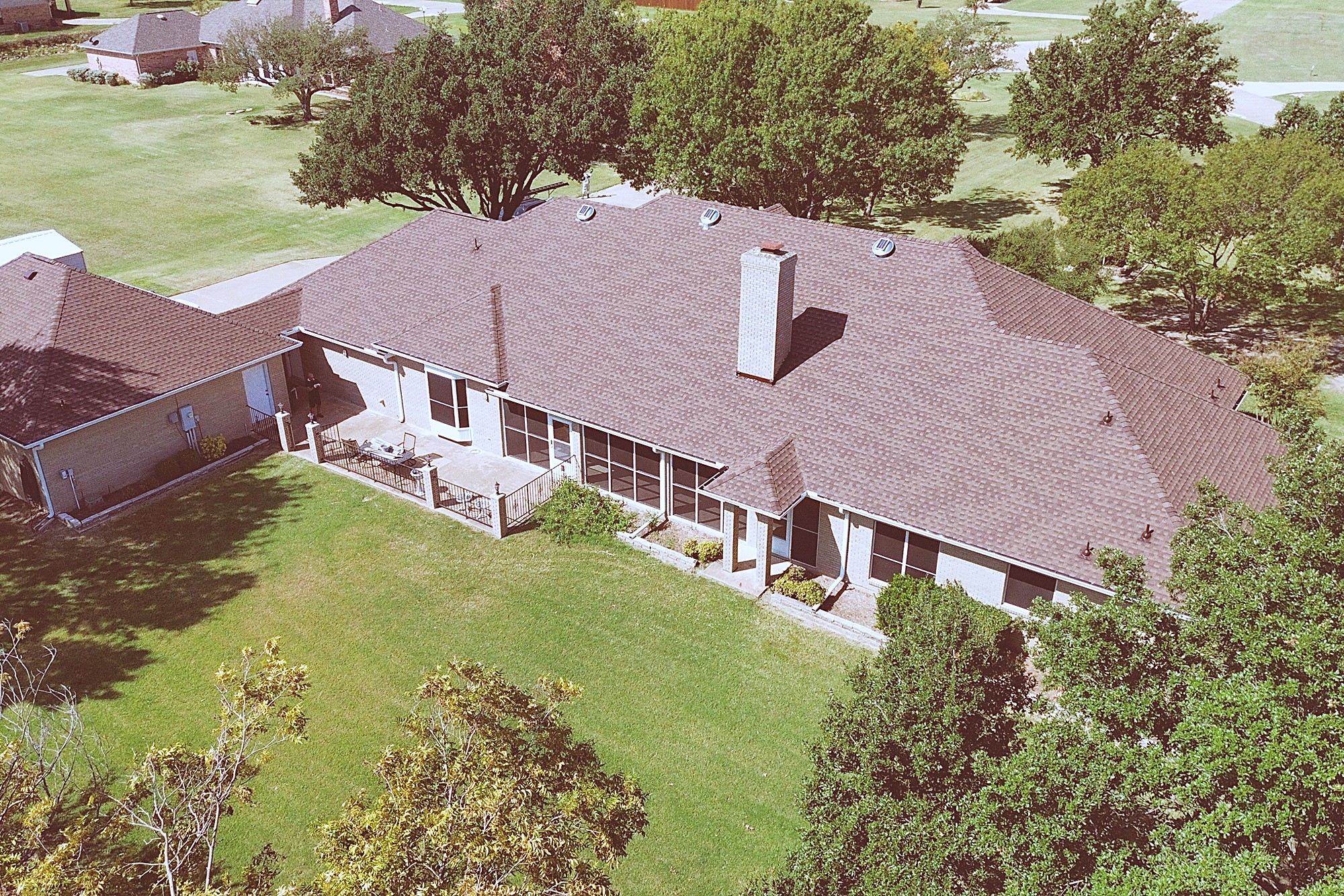 Aerial view of a ranch home with a screened porch under a new brown shingle roof
