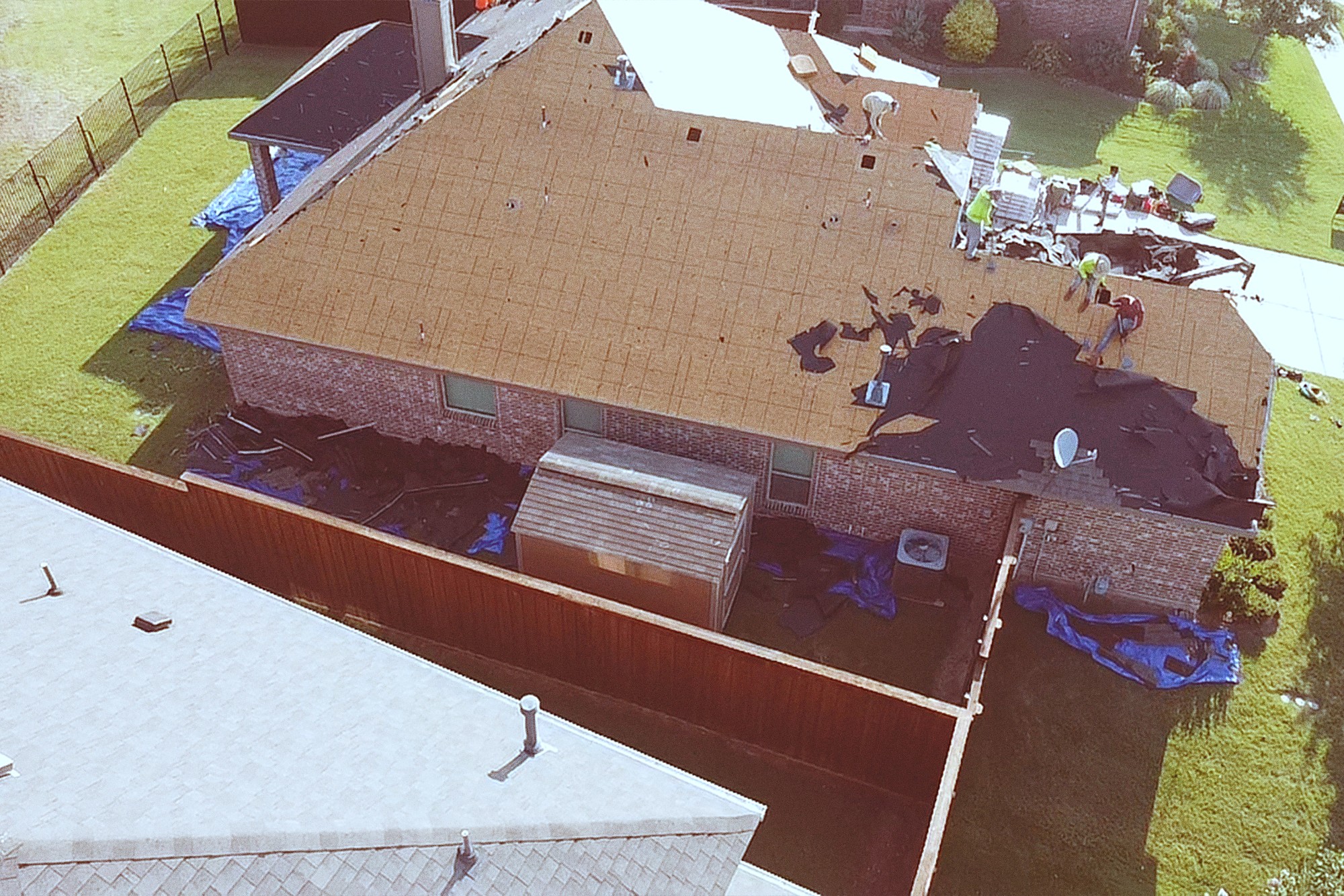 Aerial view of a crew tearing off an old roof on a single-story brick home