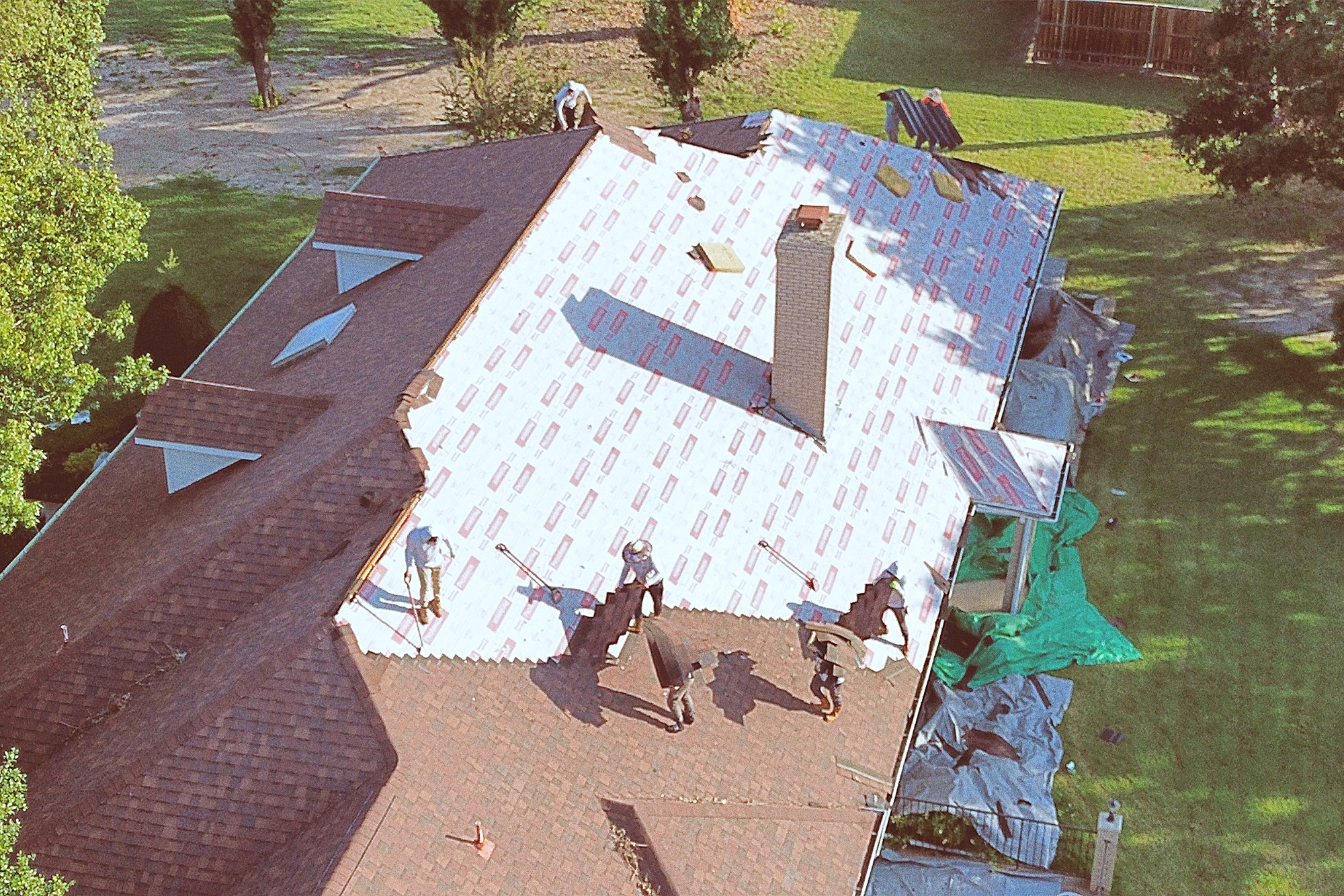 Roofers laying synthetic underlayment around a brick chimney