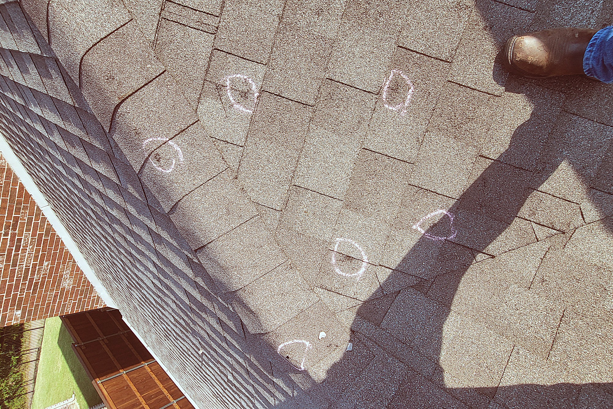Hail hits circled in chalk on a weathered shingle roof during an inspection