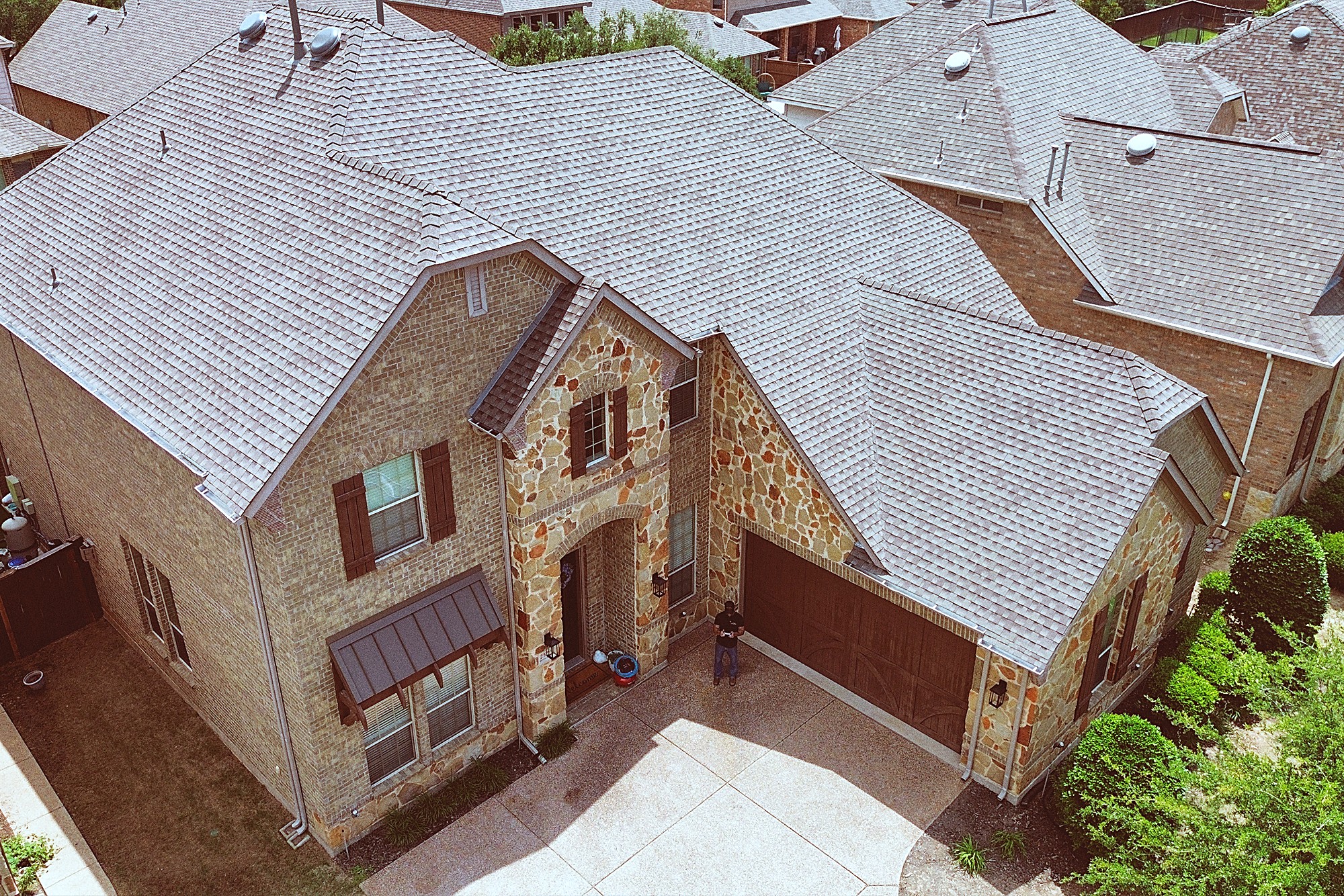 Aerial view of a stone-front two-story home with a new gray shingle roof