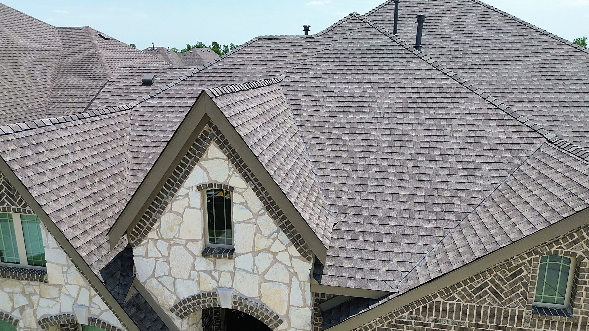 A new shingle roof over the stone and brick gables of a two-story home