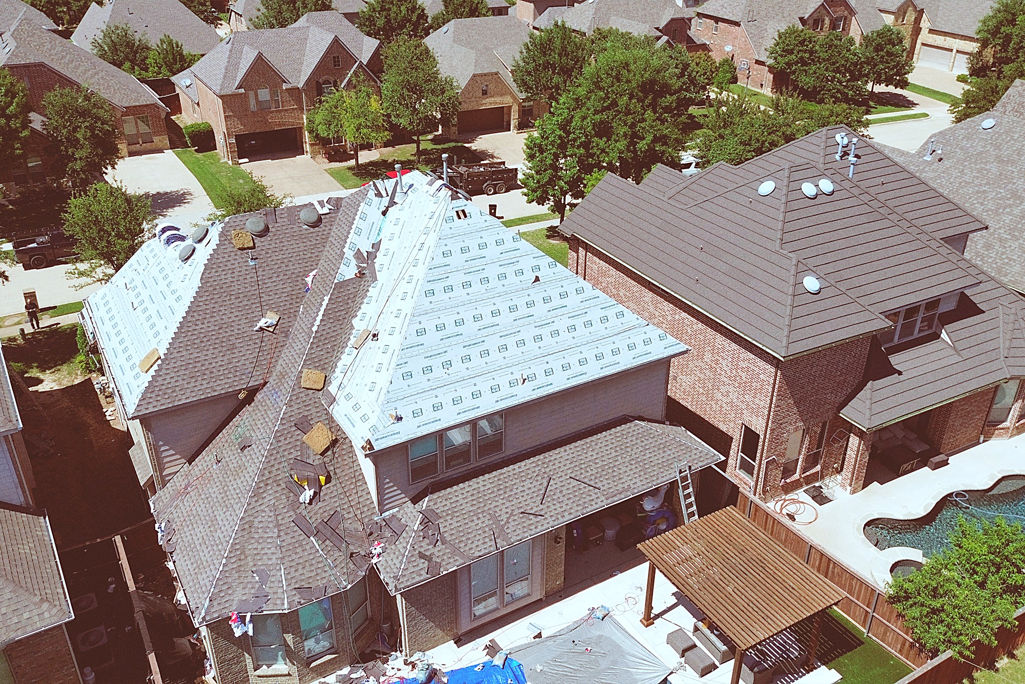 A two-story home mid-replacement with underlayment on one side, a pool next door
